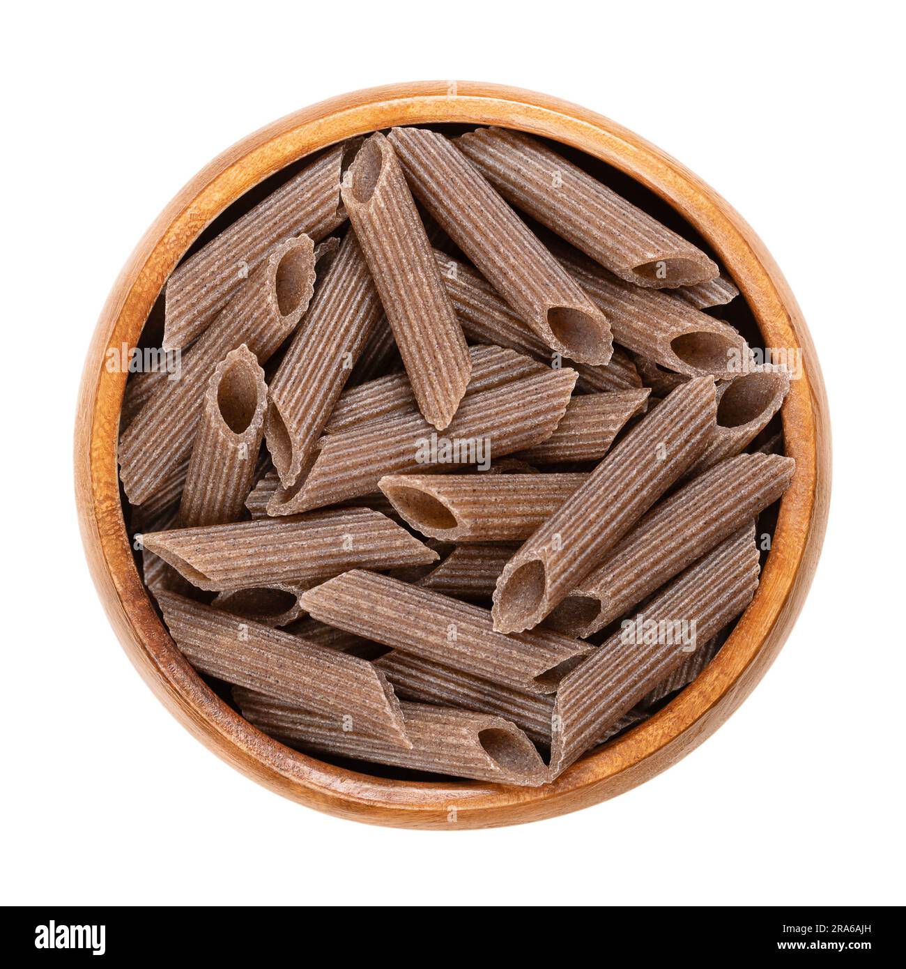 Buckwheat penne, gluten free whole grain pasta, in a wooden bowl. Dark brown noodles, made of pure buckwheat semolina, extruded into cylinder-shaped. Stock Photo