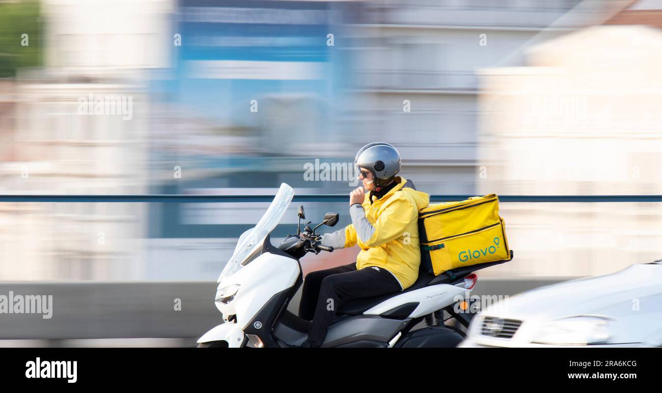 Belgrade, Serbia - May 20, 2023: Courier service delivery person working for Glovo riding a scooter with rear container in city traffic Stock Photo