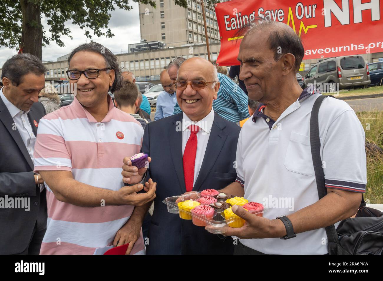 London, UK. 1 July 2023. Cakes tof everyone - including Virendra Sharma MP. Campaigners from Ealing Save Our NHS celebrated 75 years of the NHS on the side of the main road in front of Ealing Hospital. Speakers called for a proper workforce plan, pointing out the failure of the recent government plan to recognise the realities of an overworked and underpaid system which has been deliberately run into the ground as a pretext for privatisation. Peter Marshall/Alamy Live News Stock Photo