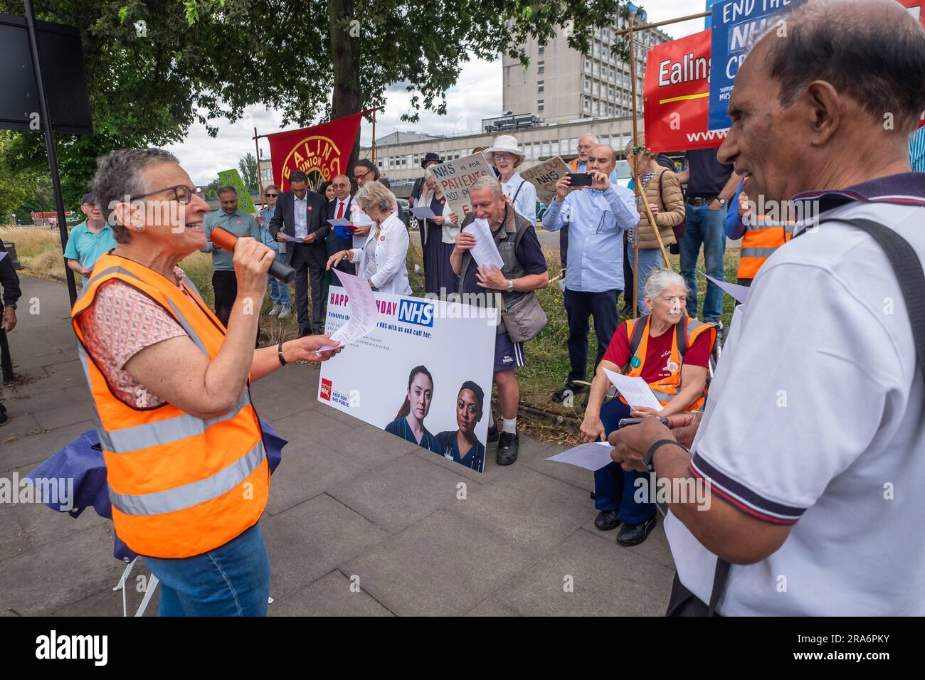 London, UK. 1 July 2023. Eve Turner, Ealing Save Our NHS, leads some singing. Campaigners from Ealing Save Our NHS celebrated 75 years of the NHS on the side of the main road in front of Ealing Hospital. Speakers called for a proper workforce plan, pointing out the failure of the recent government plan to recognise the realities of an overworked and underpaid system which has been deliberately run into the ground as a pretext for privatisation. Peter Marshall/Alamy Live News Stock Photo