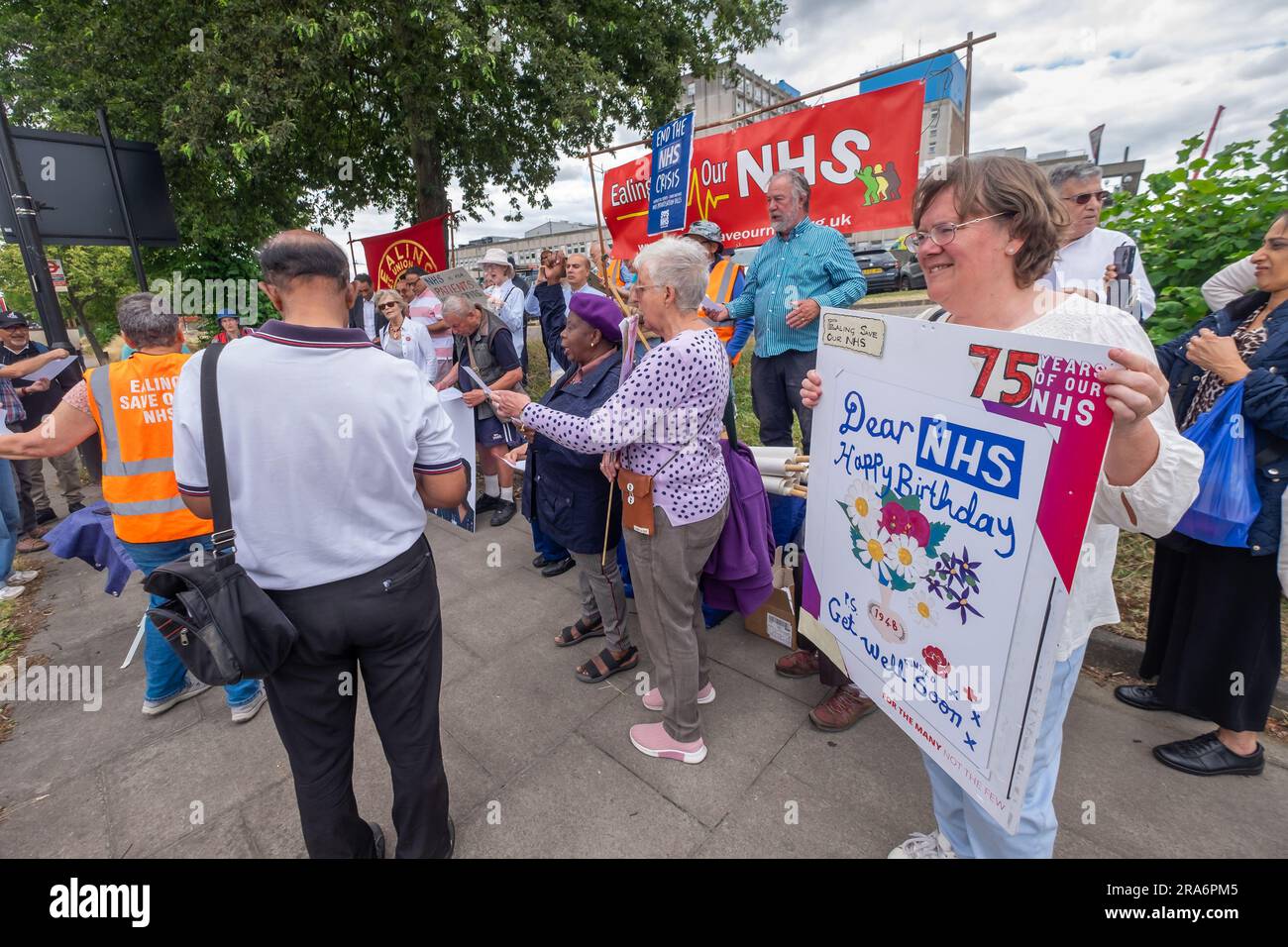 London, UK. 1 July 2023. Campaigners from Ealing Save Our NHS celebrated 75 years of the NHS on the side of the main road in front of Ealing Hospital. Speakers called for a proper workforce plan, pointing out the failure of the recent government plan to recognise the realities of an overworked and underpaid system which has been deliberately run into the ground as a pretext for privatisation. Peter Marshall/Alamy Live News Stock Photo