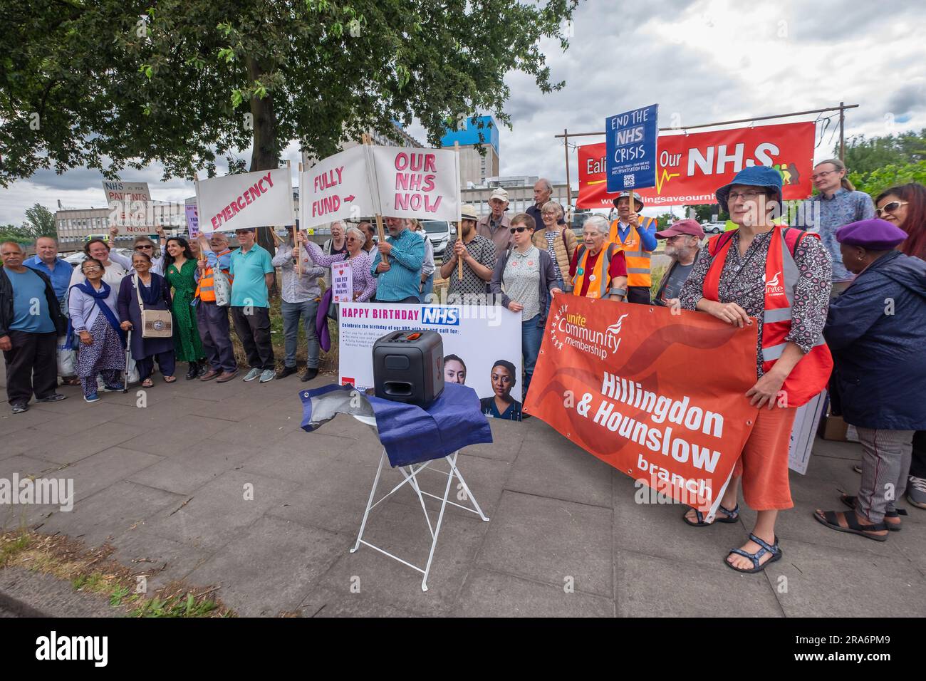 London, UK. 1 July 2023. Campaigners from Ealing Save Our NHS celebrated 75 years of the NHS on the side of the main road in front of Ealing Hospital. Speakers called for a proper workforce plan, pointing out the failure of the recent government plan to recognise the realities of an overworked and underpaid system which has been deliberately run into the ground as a pretext for privatisation. Peter Marshall/Alamy Live News Stock Photo