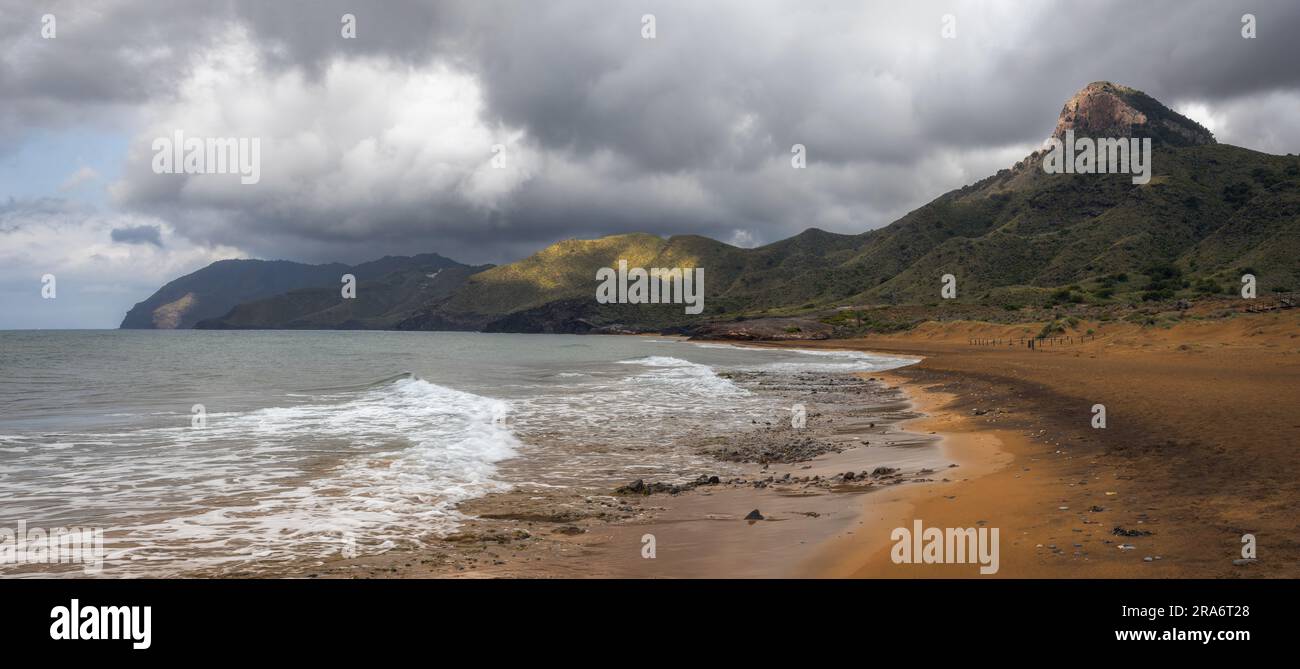 Serene beach, golden sand, gentle waves,  and stunning coastal scenery at Calblanque Regioanl Park, Murcia Spain Stock Photo