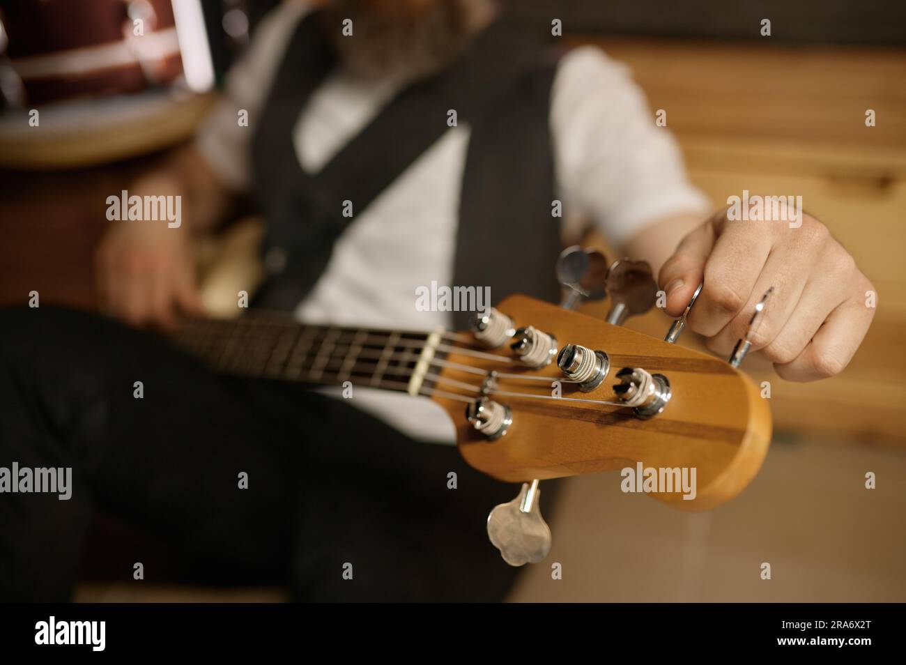 Bearded brutal guitarist tuning his musical instrument while sitting on floor Stock Photo