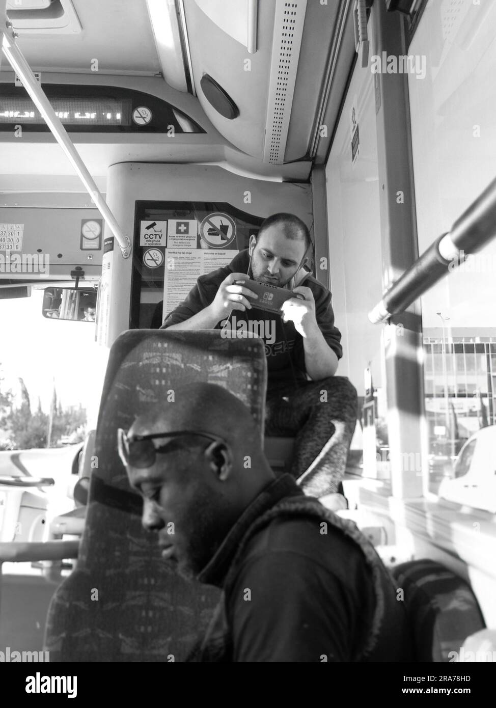 black and white young man sitting on public bus and playing with video games, Valletta, Malta Stock Photo