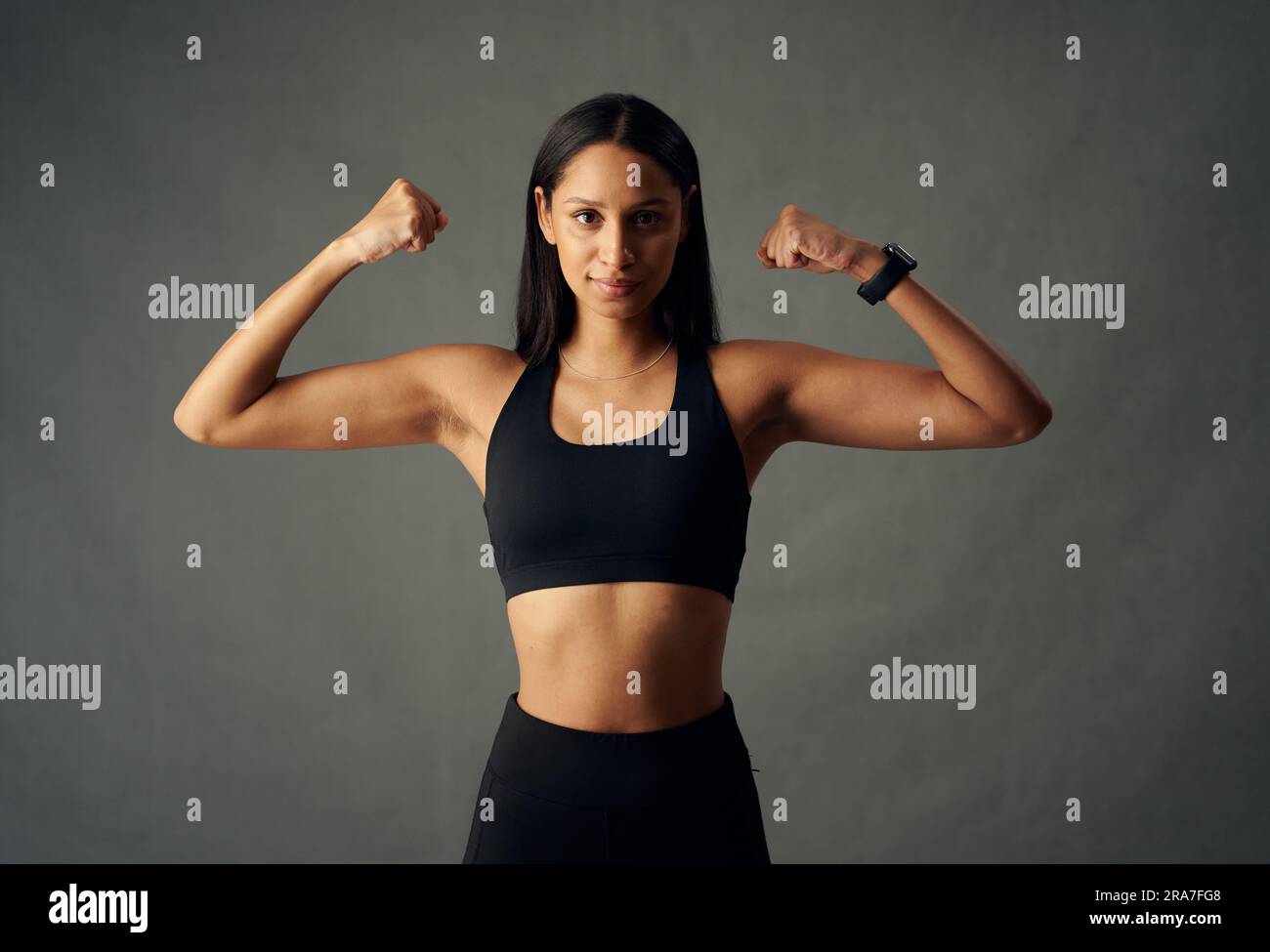 Young biracial woman wearing sports bra and fitness tracker flexing