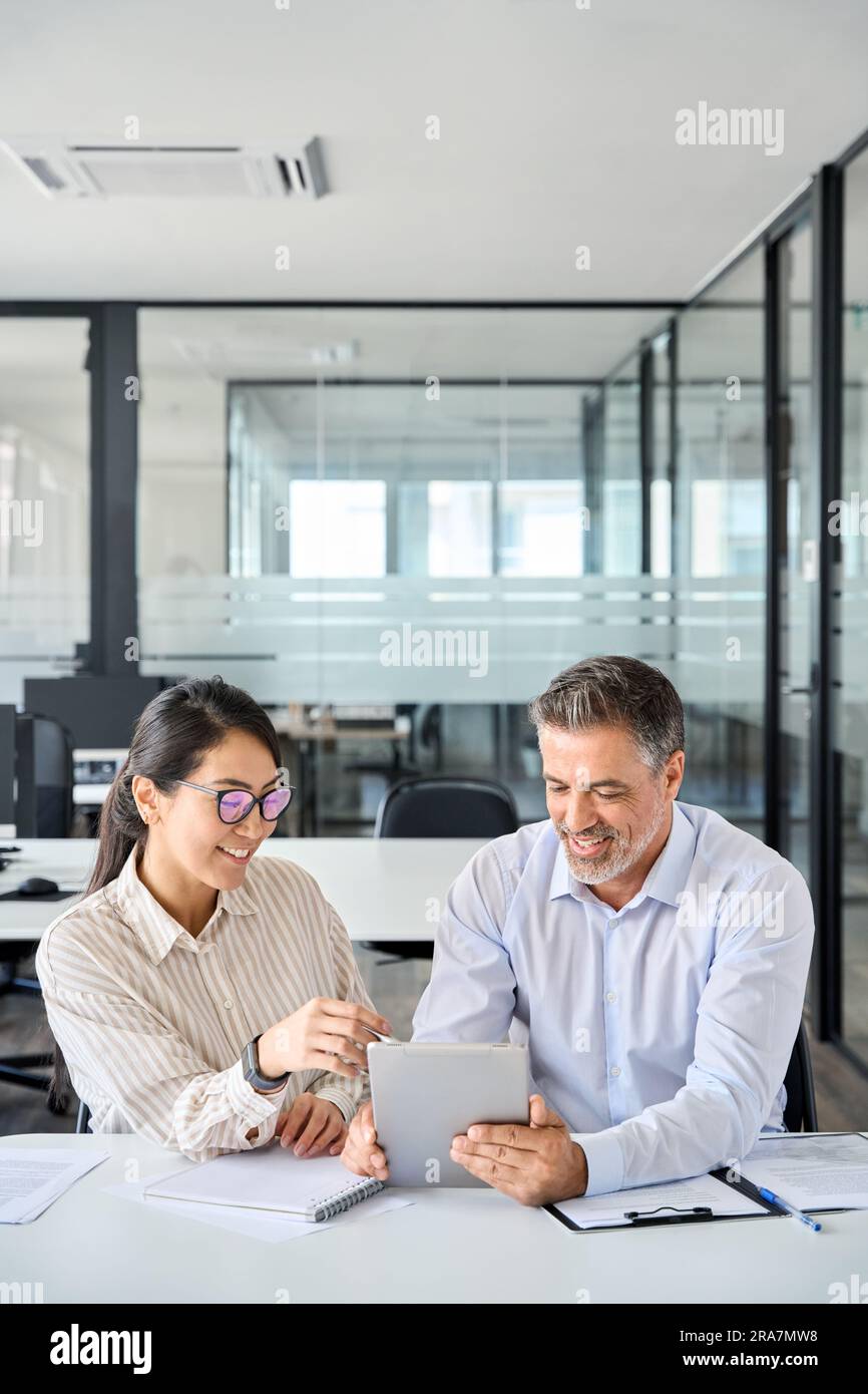 Two diverse business team people talking working using digital tablet in office. Stock Photo