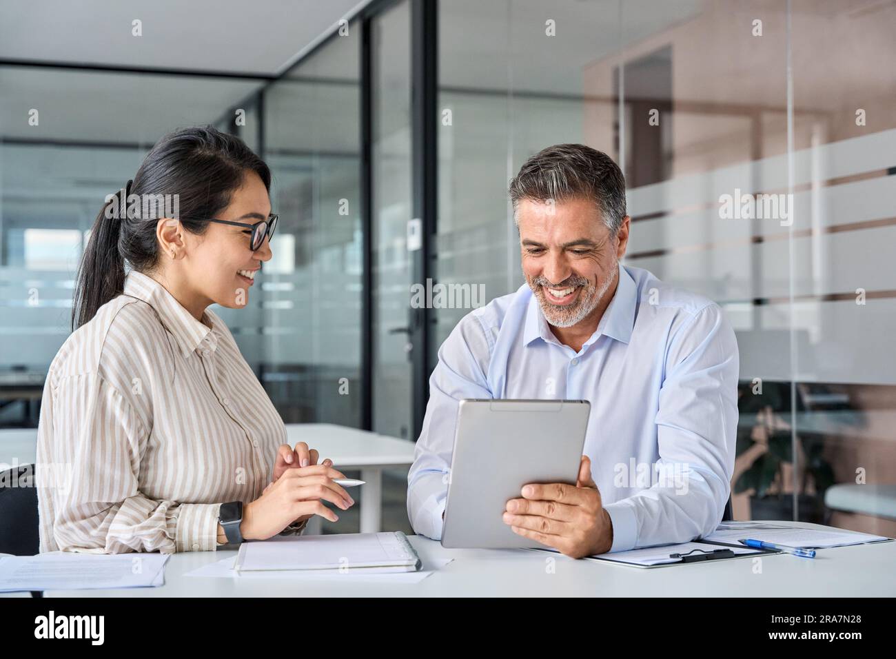 Two happy diverse executives discussing work using digital tablet in office. Stock Photo