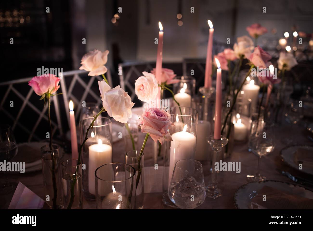 Chivalric wedding with pillars of candles and roses in glass vases. Lush garden arrangements decorating pillars by chairs. Tableware settings + bokeh. Stock Photo