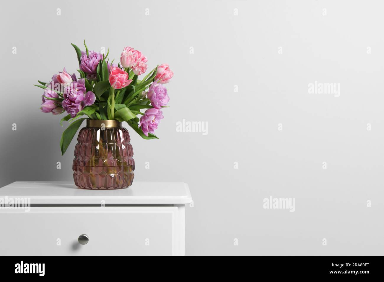Beautiful bouquet of colorful tulip flowers on white bedside table near