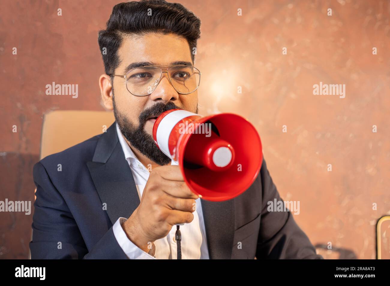 Young indian businessman in suit and glasses shouting in megaphone