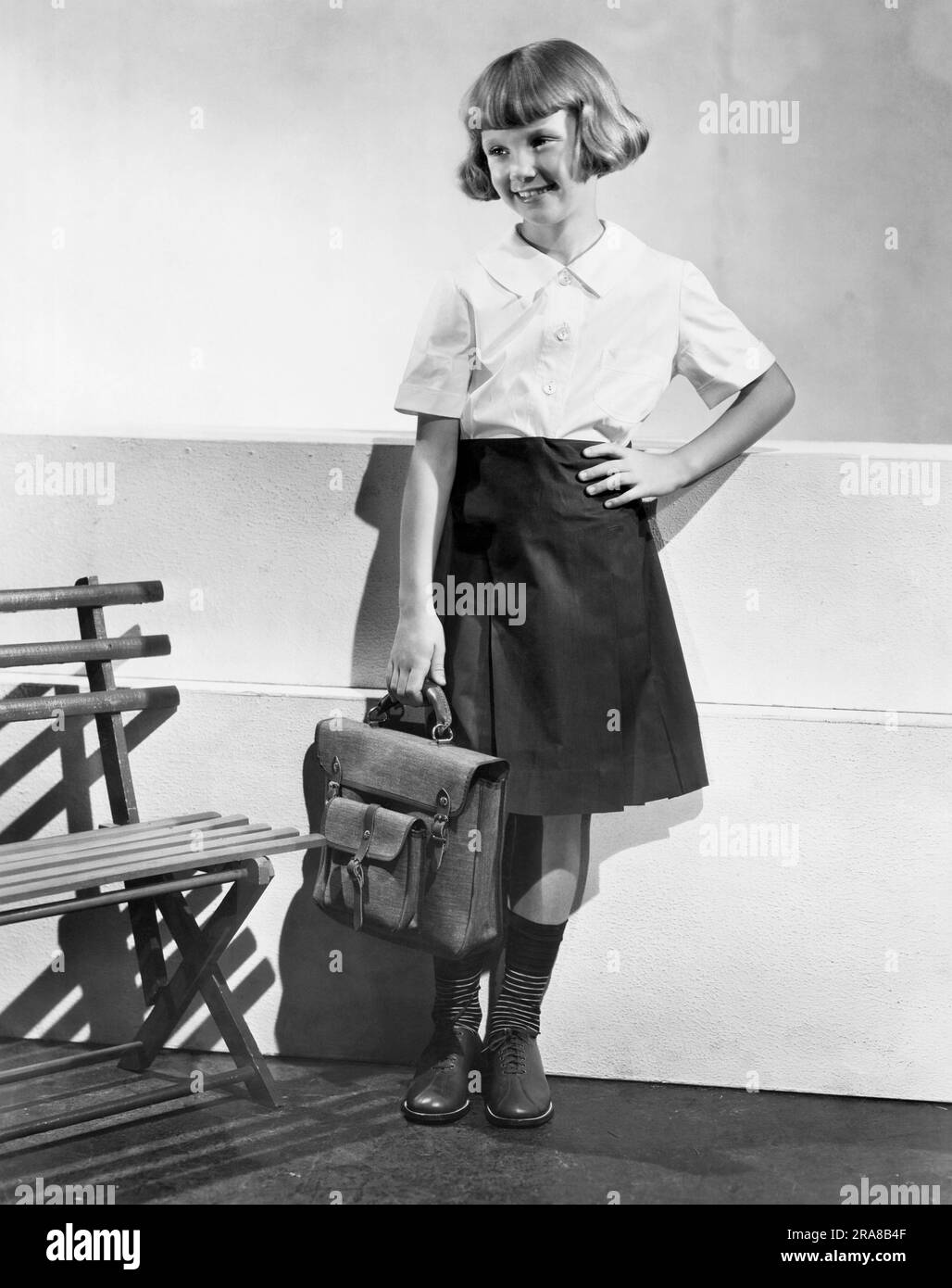 United States:  September, 1933 A fashionable young girl holding a book bag and wearing school clothes that were sewed at home. Stock Photo