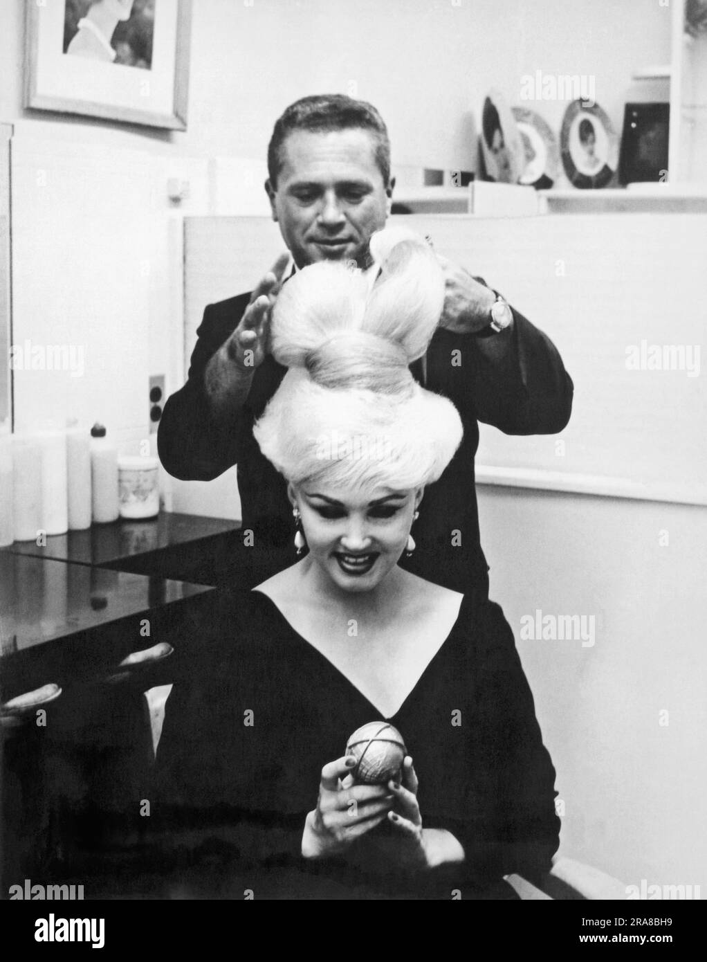 New York, New York:  1964. Stylist John Fonda puts the finishing touches on 'The Unisphere Hairdo', on Ecstasy, a featured stripper in the Broadway play, 'This Was Burlesque'. The hair was inspired by the official symbol of the 1964 NY World's Fair. Stock Photo
