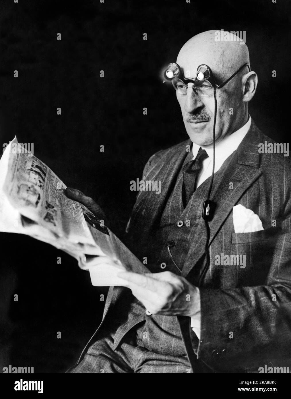 Berlin, Germany:  c. 1926 A man using a new electric attachment for glasses for reading at night. It has tiny electric bulbs and runs off of dry cells, and was invented by an optician here. Stock Photo
