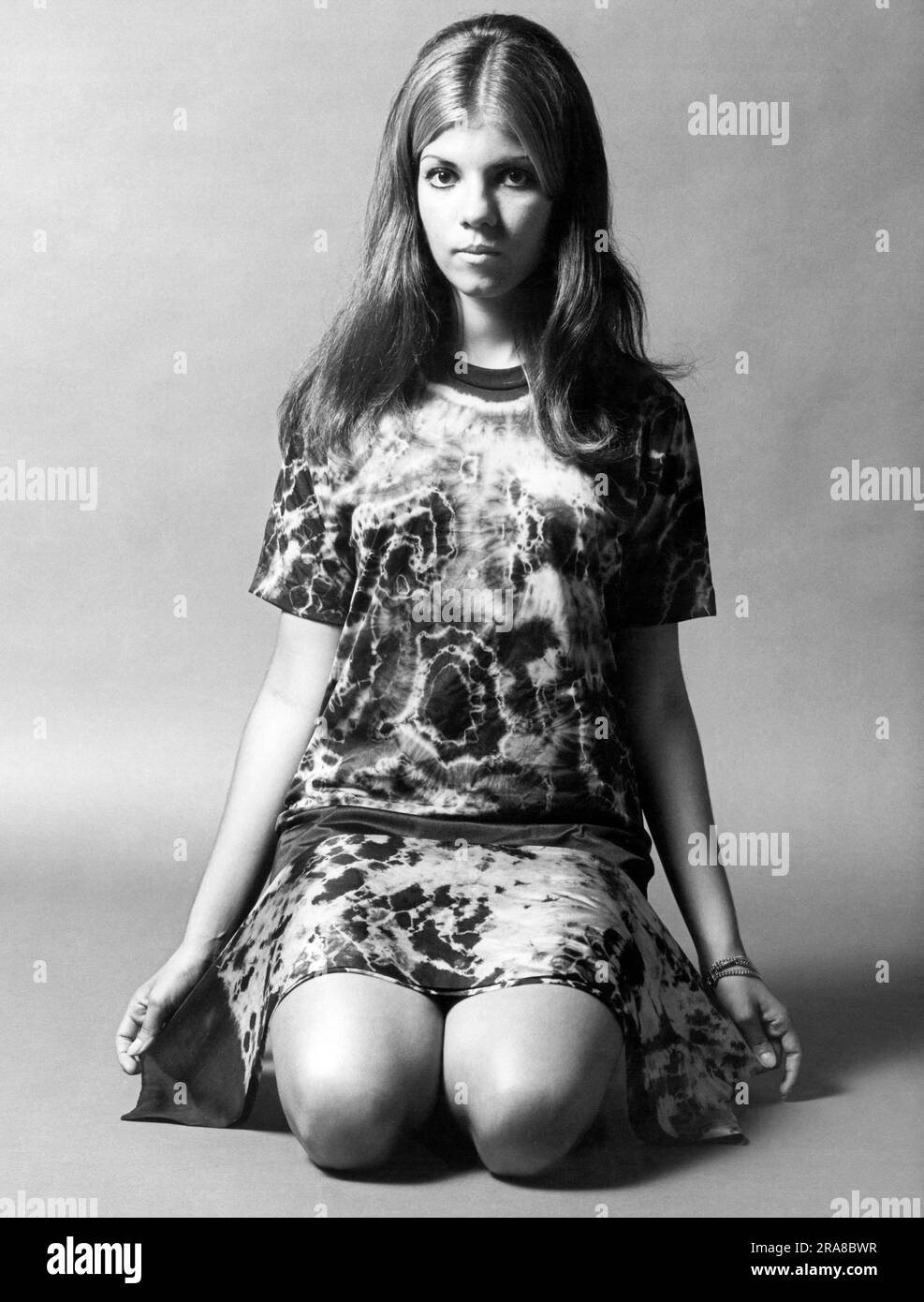 United States:   1969 A young woman kneeling and wearing a tie-dyed shirt with a tie-dyed scarf draped across her legs. Stock Photo