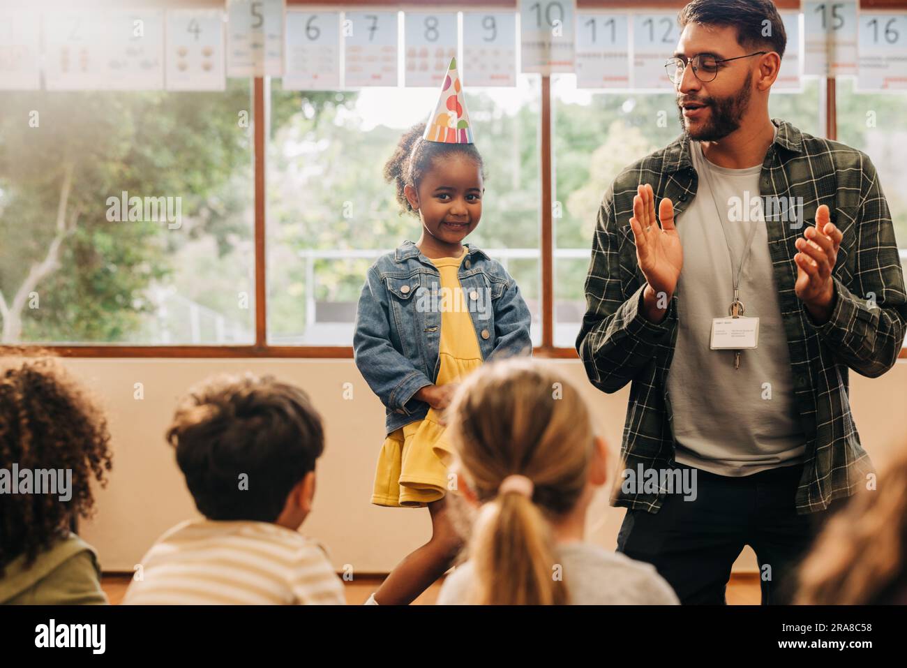 birthday celebration at primary school class. Little black girl is celebrating her birthday with her classmates and teacher. Fun and child growth in e Stock Photo