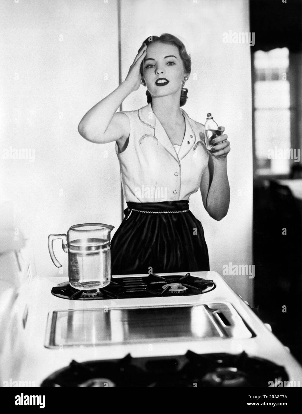 United States:  July, 1951 In this photograph from the Frangrance Foundation, 'Despite the heat from the stove in the summertime, this young homemaker will appear crisp and pretty at mealtime thanks to kitchen fresh-ups with cooling cologne.' Stock Photo