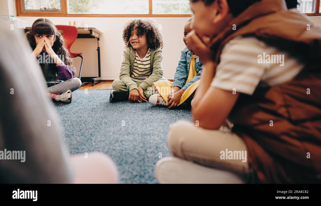 Group of children sitting in a circle in a classroom. Boys and girls enjoy learning in school, they listen their educator during a lesson. Kids school Stock Photo