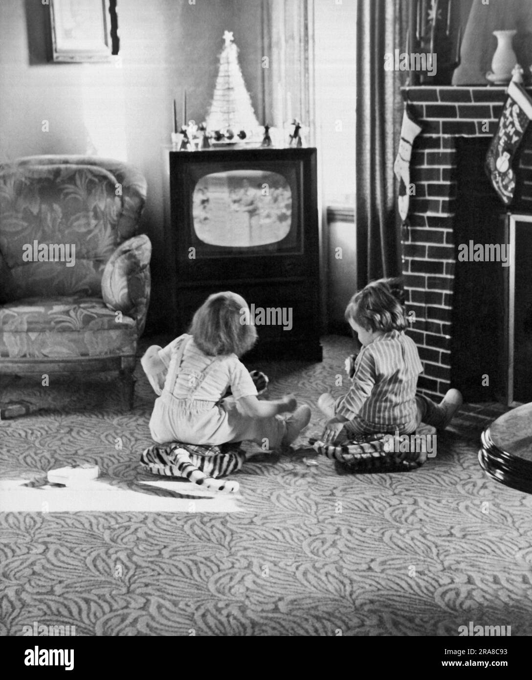 United States:  c. 1955, Two small children sitting on the living room floor watching television. Stock Photo