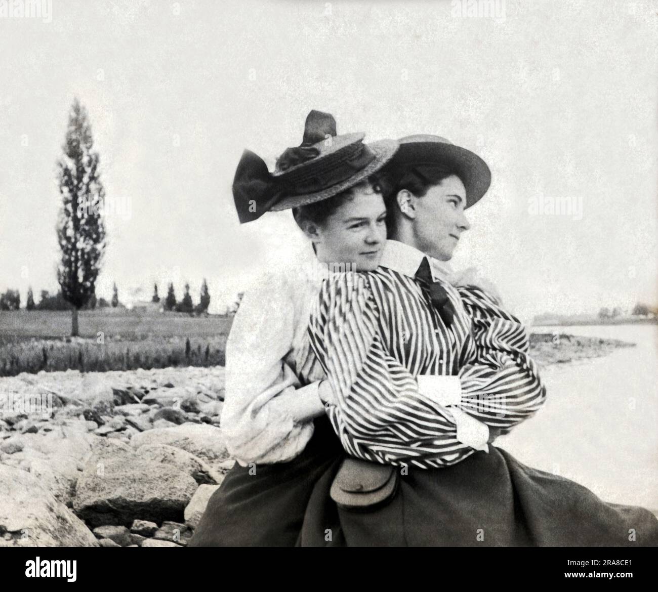 United States:  1896 Two young Victorian women snuggle by a stream in the countryside. Stock Photo