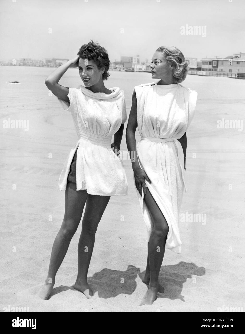 England:  1954   Terry-cloth coverups look delightful on these two models standing on a beach. Stock Photo