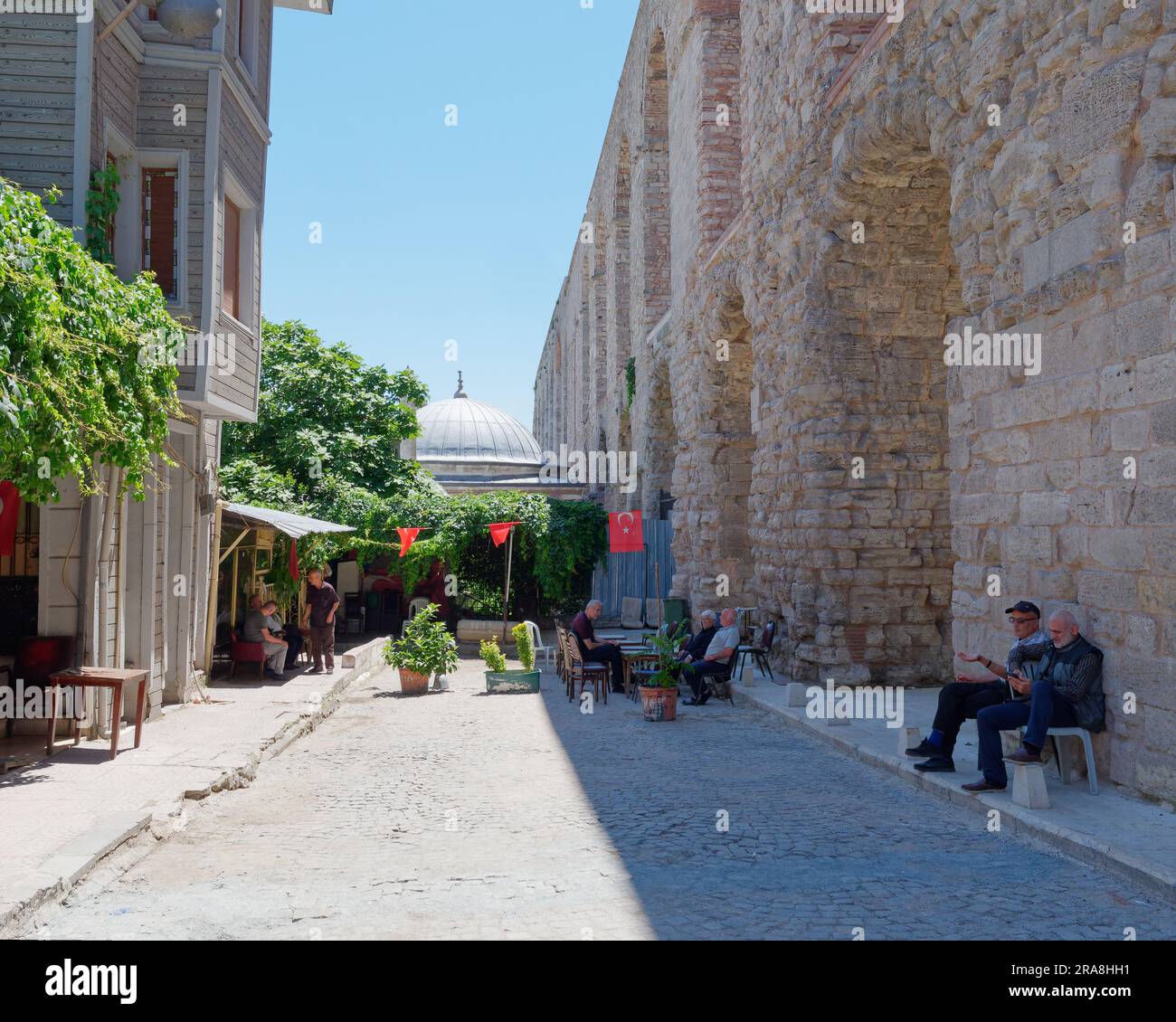 Locals sitting in the shade on a street beside the Aqueduct of Valens, a Roman Aqueduct in Istanbul, Turkey Stock Photo