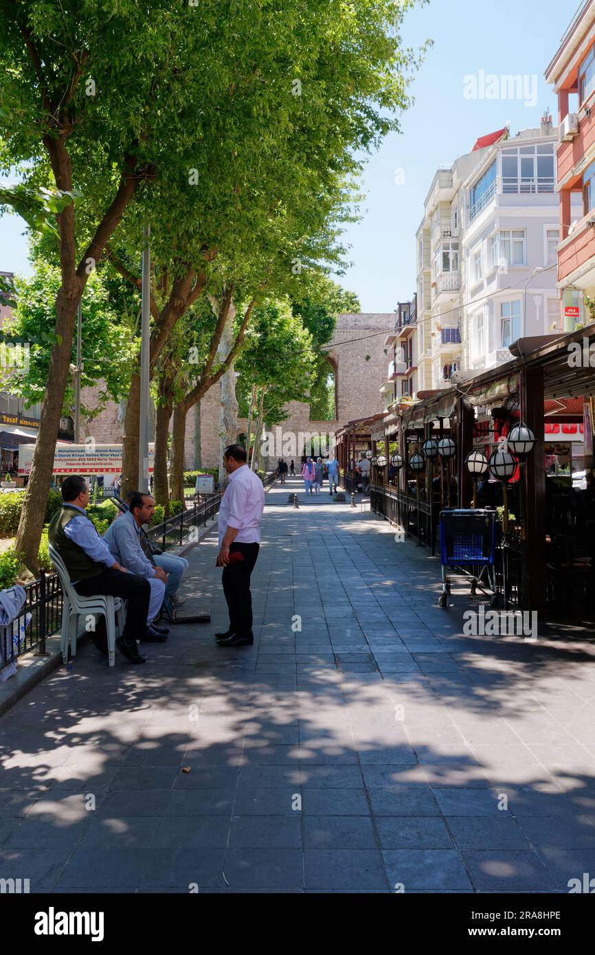 Locals sitting and socialising on a street beside the Aqueduct of Valens, a Roman Aqueduct in Istanbul, Turkey Stock Photo