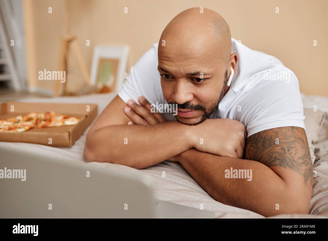 Closeup of adult black man watching videos via laptop laying in bed at home during lazy weekend Stock Photo