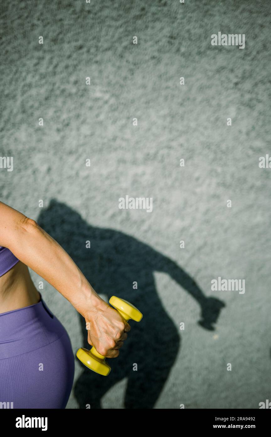 Crop sportswoman doing exercise with colorful dumbbell Stock Photo