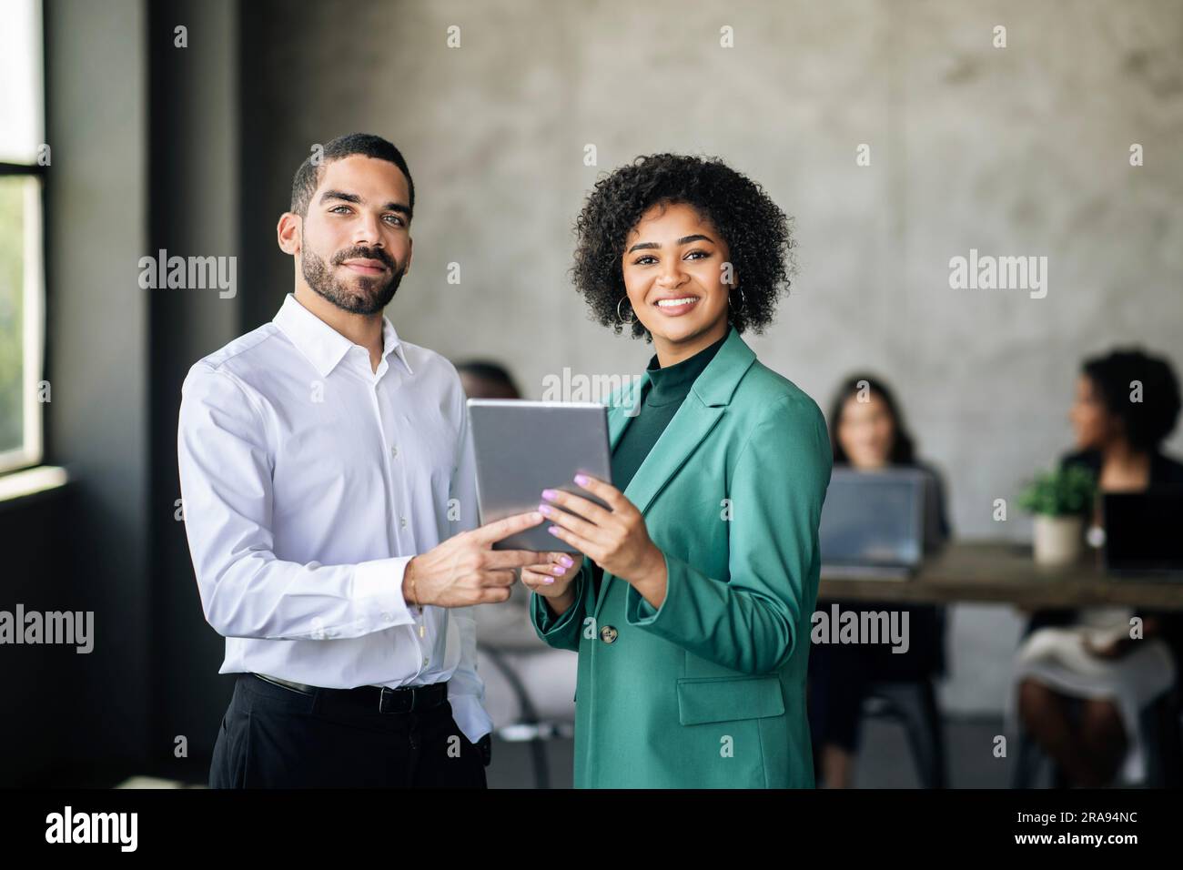 Two Happy Hispanic Colleagues Posing With Digital Tablet In Office Stock Photo