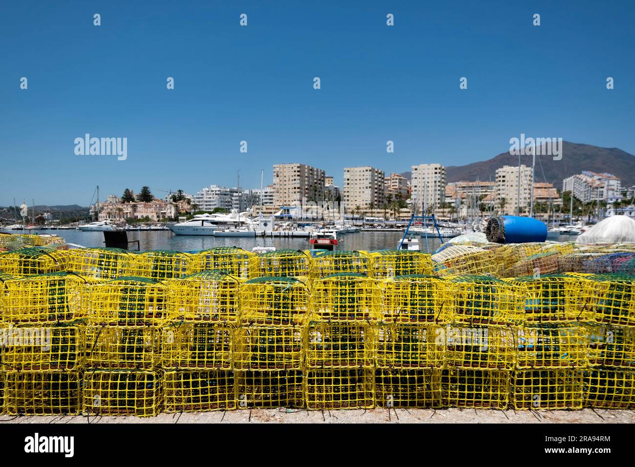 Stacked up colourful lobster pots or crab boxes line the side of the old port, Estepona Spain with the new town marina shown in the background Stock Photo