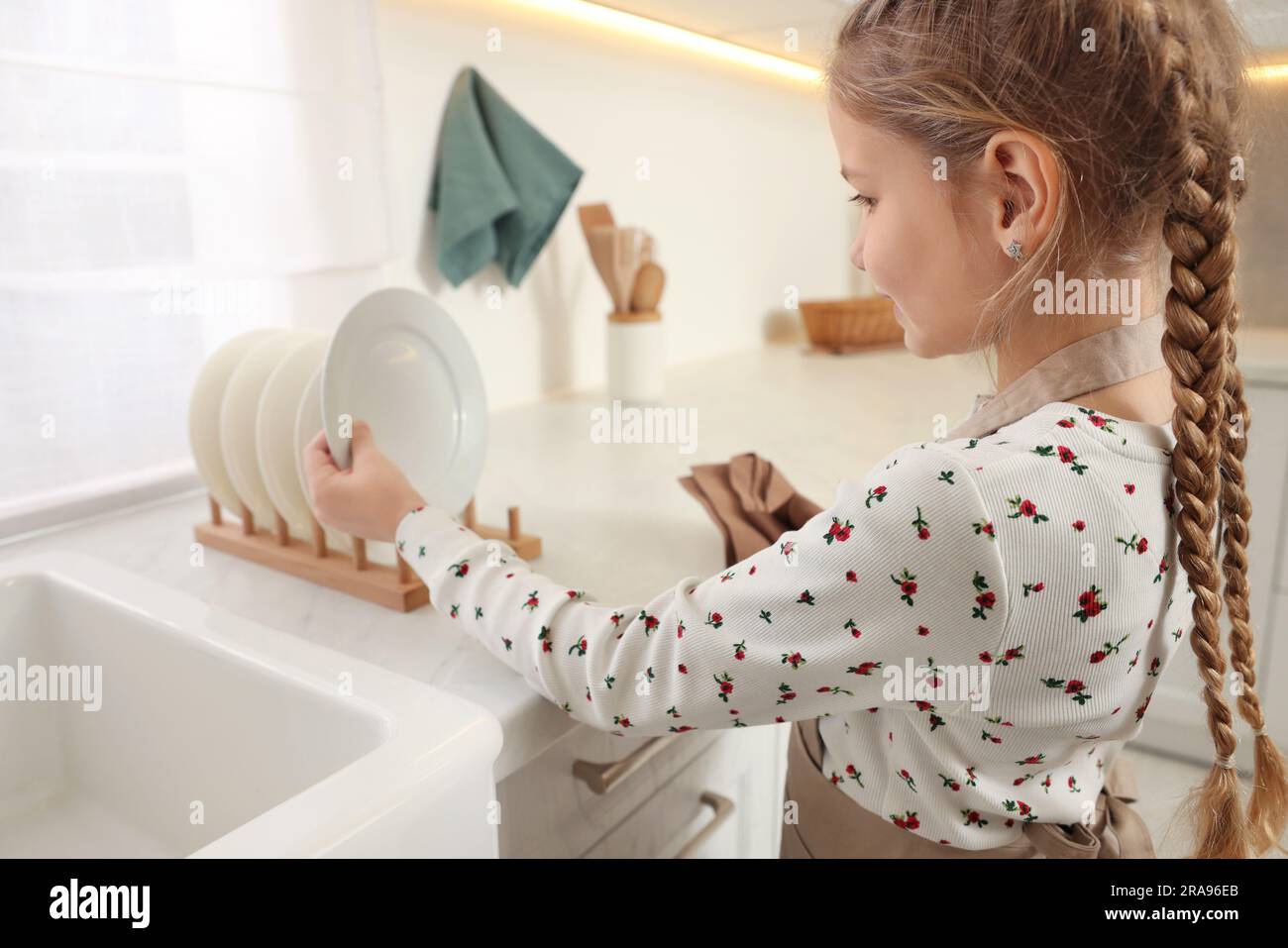 Girl putting clean plate on drying rack in kitchen Stock Photo