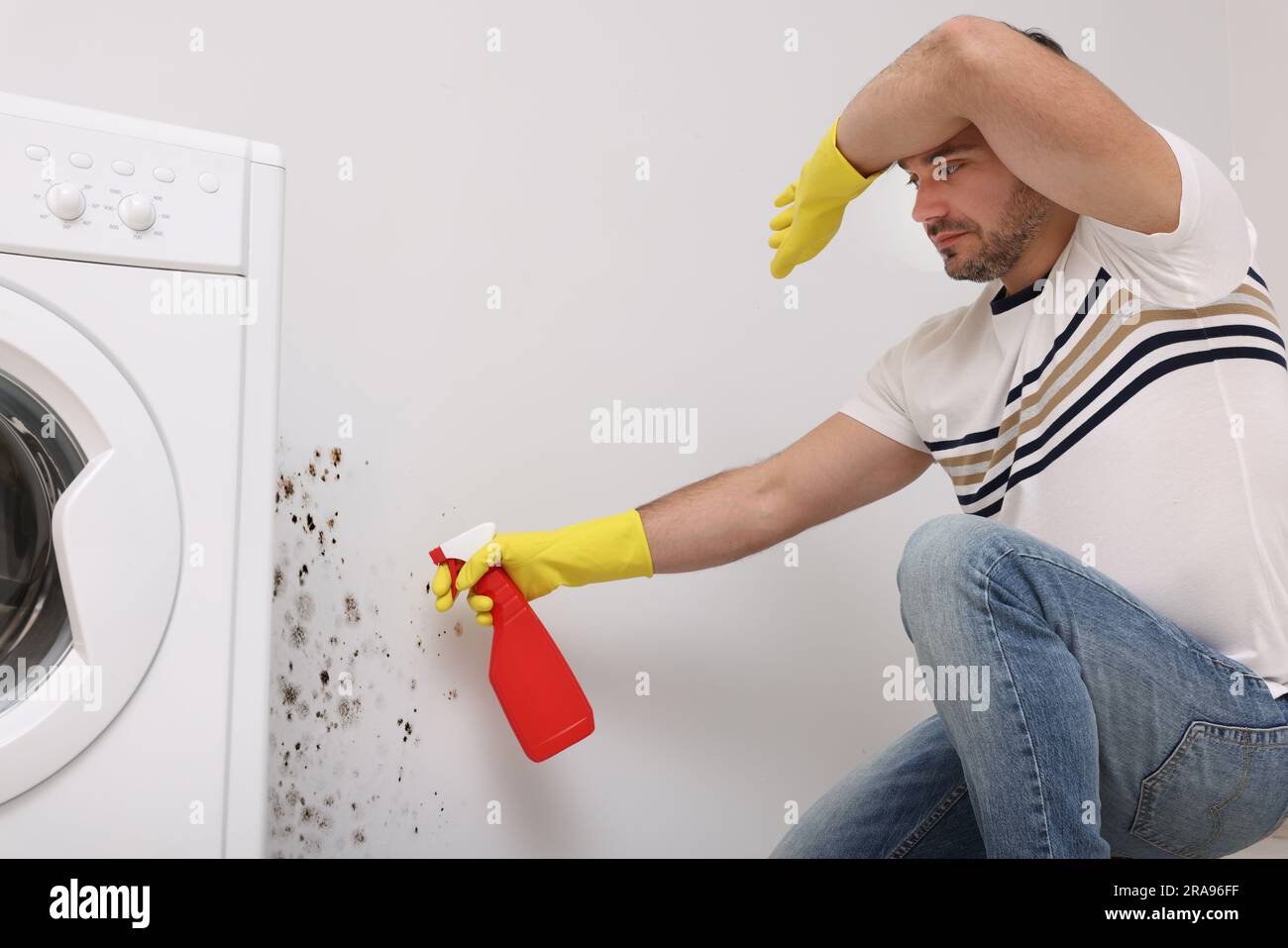 Man in rubber gloves using mold remover on wall in bathroom Stock Photo