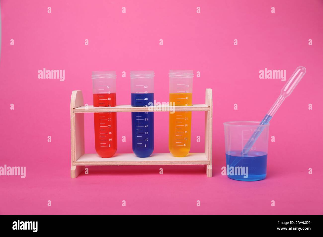 Beaker and test tubes with colorful liquids in wooden stand on bright