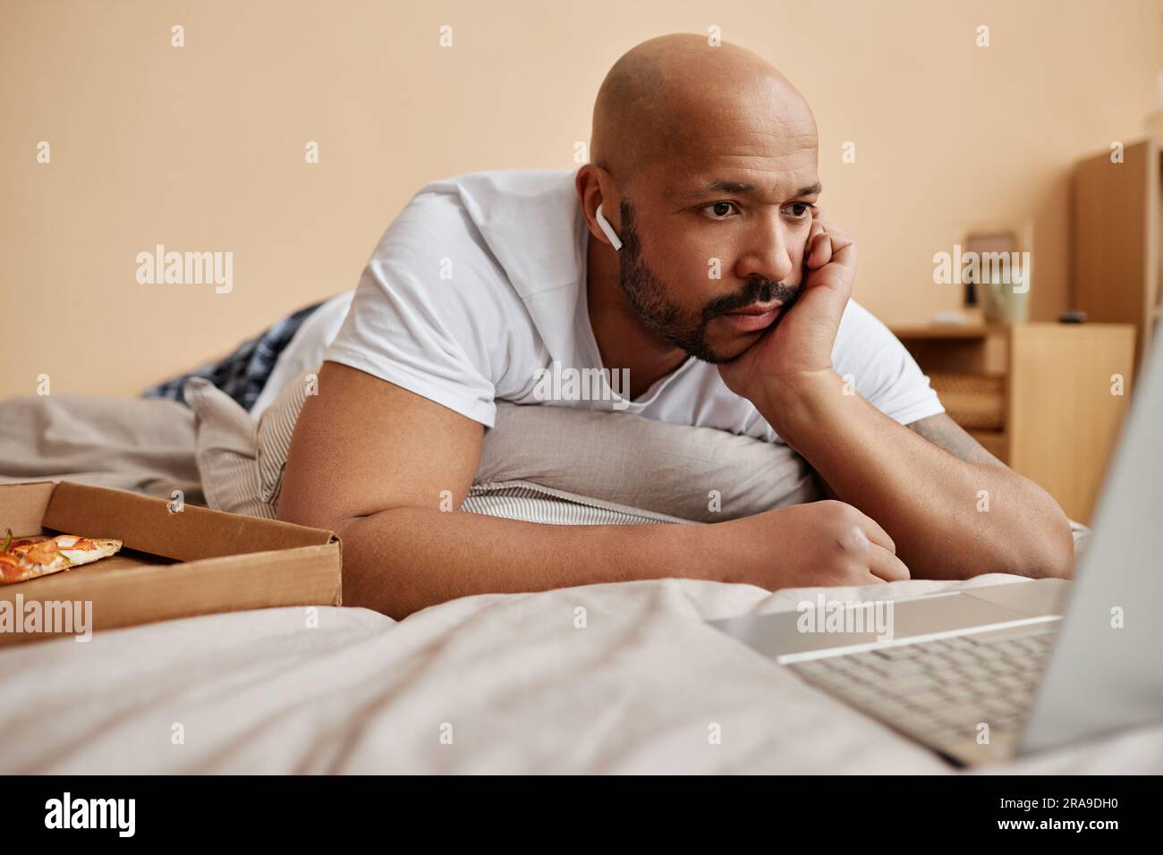 Portrait of black adult man lying in bed at home and watching movies during lazy weekend, copy space Stock Photo