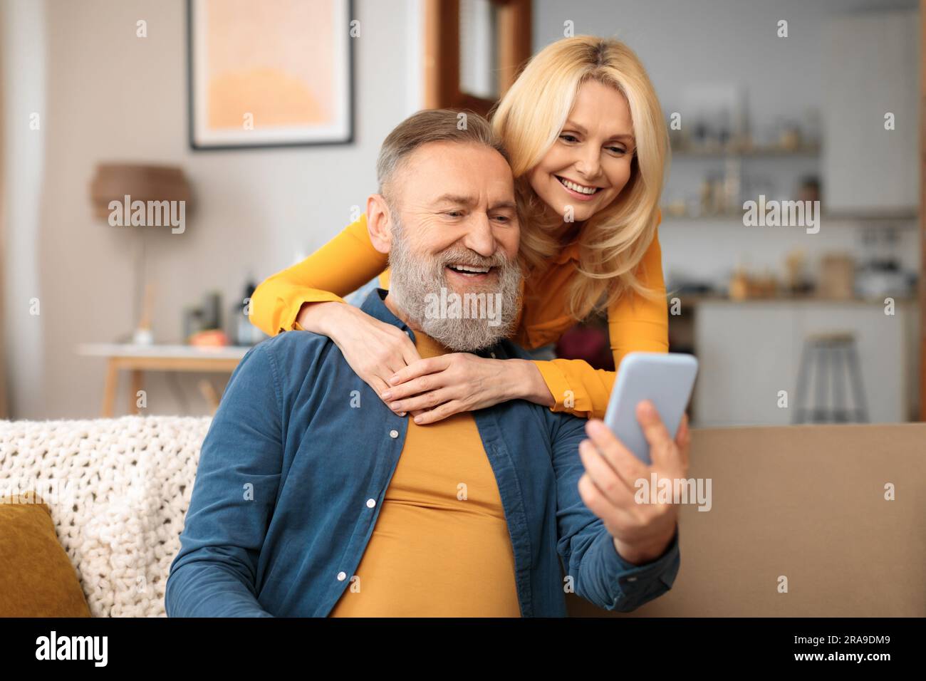Happy Mature Spouses Using Mobile Phone With Application At Home Stock Photo