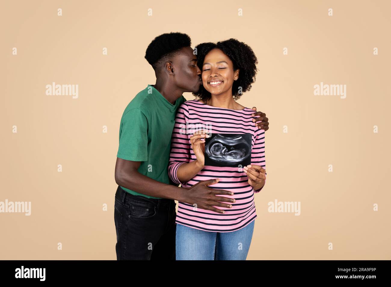 Happy young african american husband kissing cheek pregnant wife with ...