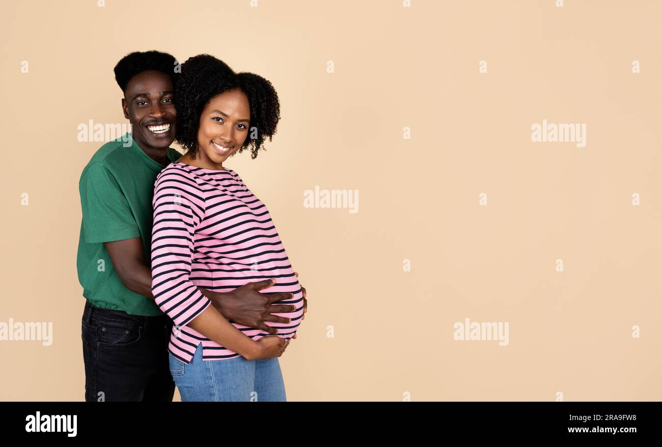 Smiling young african american husband hugging pregnant wife in casual ...