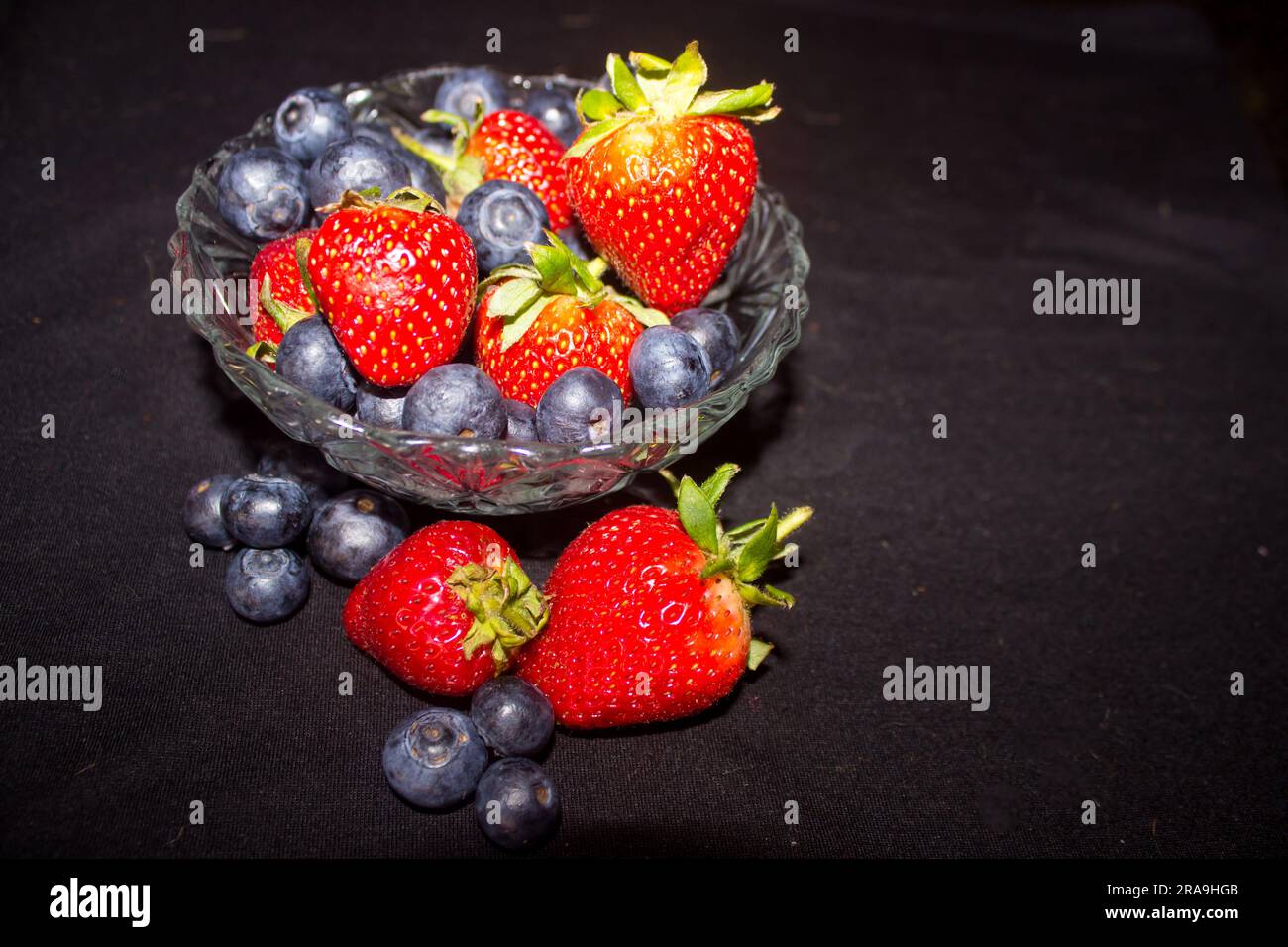 Bowl of summer berries, Strawberries and blueberries, against a black background Stock Photo