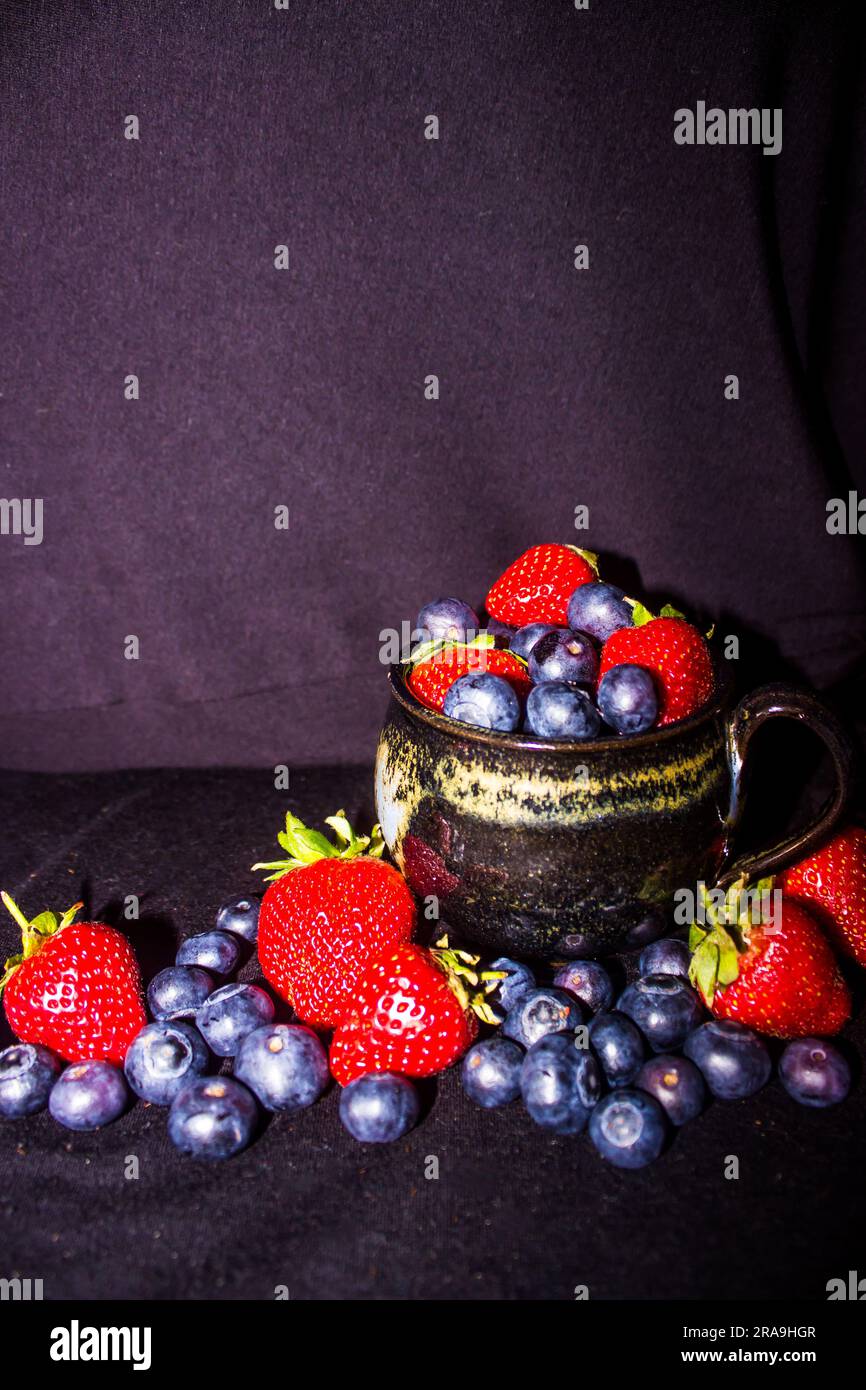 Black teacup filled to overflow with strawberries and blueberries Stock Photo
