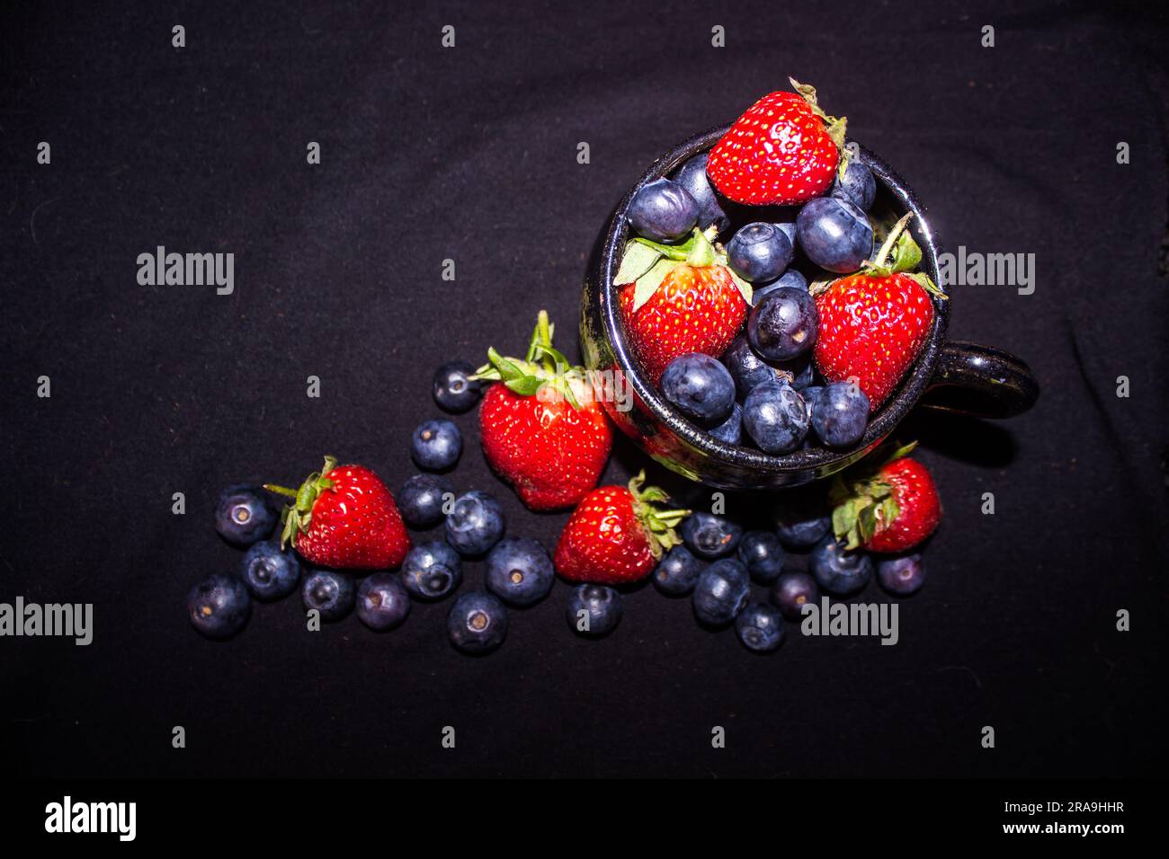 Composition of a teacup filled with blueberries and strawberries viewed from directly above against a black background Stock Photo