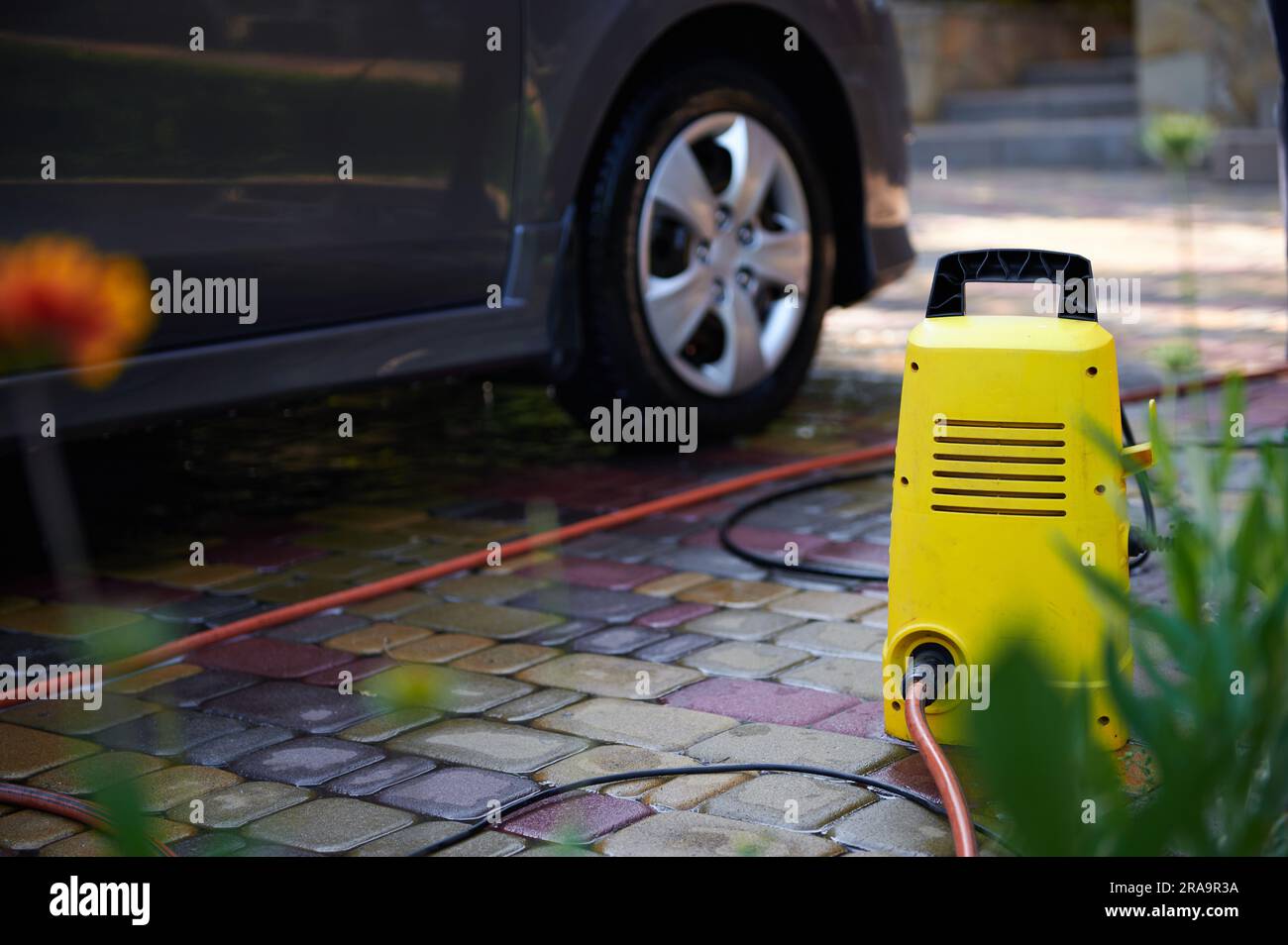 Focus on a bright yellow car cleaning equipment near a car. Water high pressure cleaner, washer