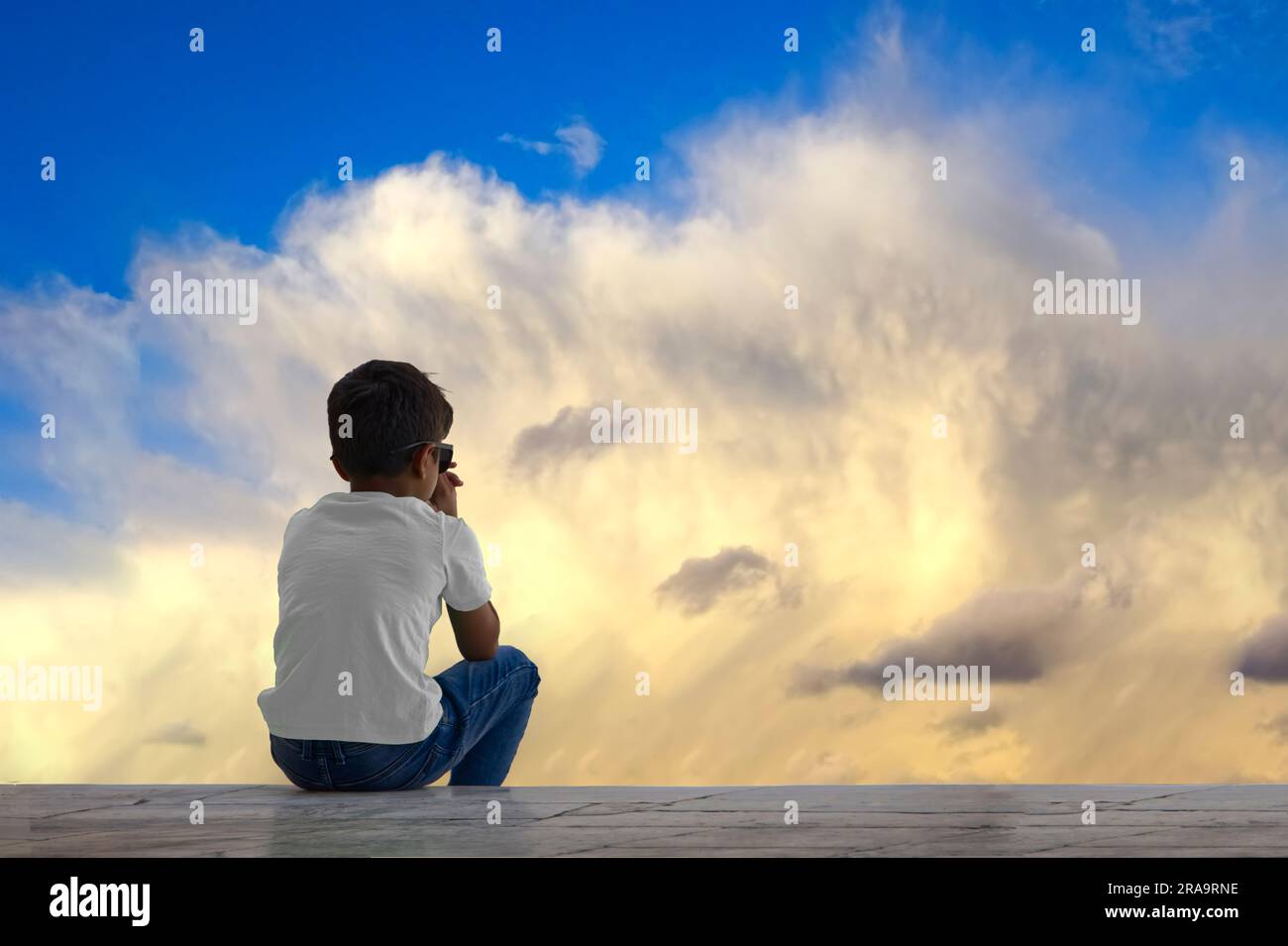 Young boy sitting and watching at the heavy clouds, that seems like waves Stock Photo