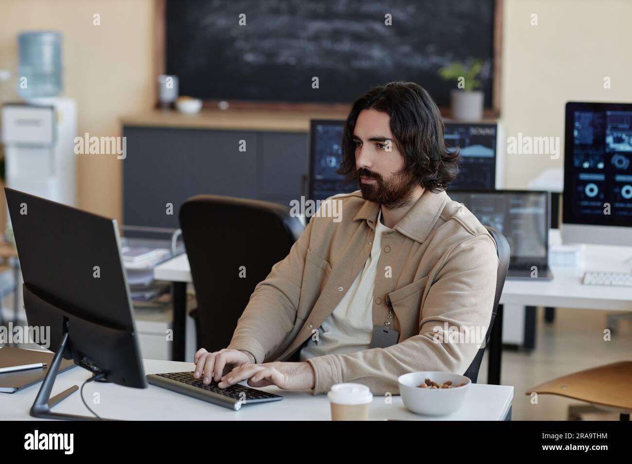 Young serious businessman typing on keyboard and looking at computer screen while analyzing data or creating new algorithms or software Stock Photo