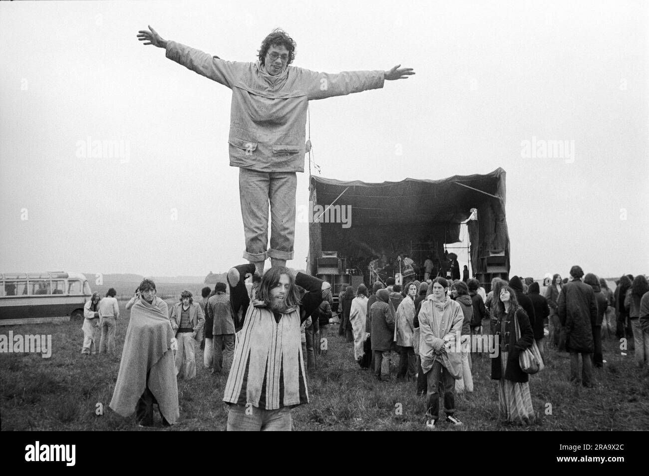 Stonehenge Free Festival at the June 21st Summer Solstice, Festival goers, its raining and cold, a band is on stage. Wiltshire, England circa June 1976. 1970s UK HOMER SYKES Stock Photo