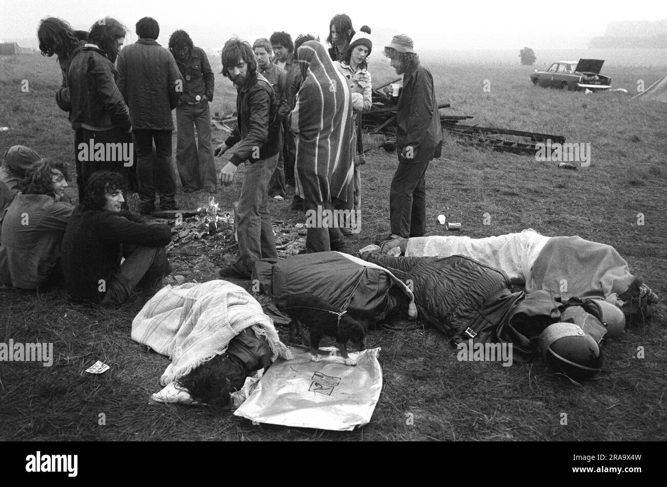 June 21st Summer Solstice. Stonehenge Free Festival at the summer solstice,  Festival goers up all night huddle around a camp fire, while others try and sleep in their sleeping bags. Wiltshire, England circa June 1976. 1970s UK HOMER SYKES Stock Photo
