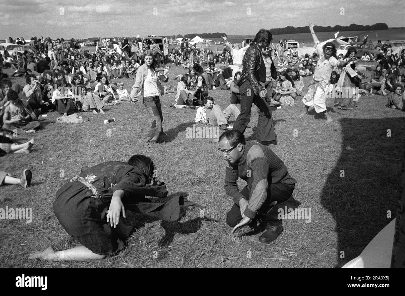 Festival goers dancing, others sitting around watching. Stonehenge Free Festival at the summer solstice, Wiltshire, England circa June 1976. 1970s UK HOMER SYKES Stock Photo