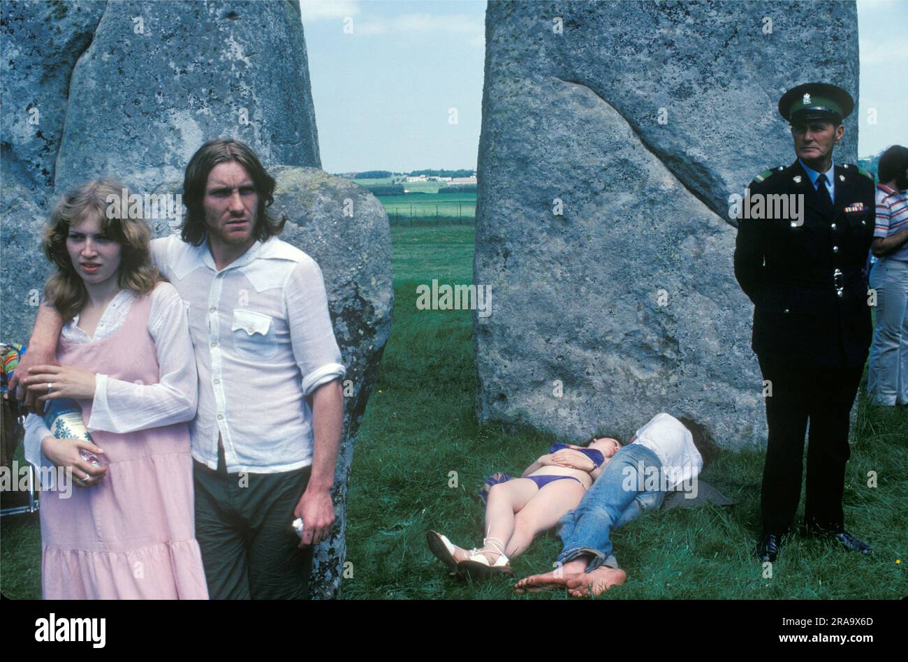 Stonehenge Free Festival at the summer solstice, Wiltshire, England June 21st 1979. Besides the hippies a small group of English tourists watched as others lay in the sun and a 'guard' stood by watching. 1970s UK HOMER SYKES Stock Photo