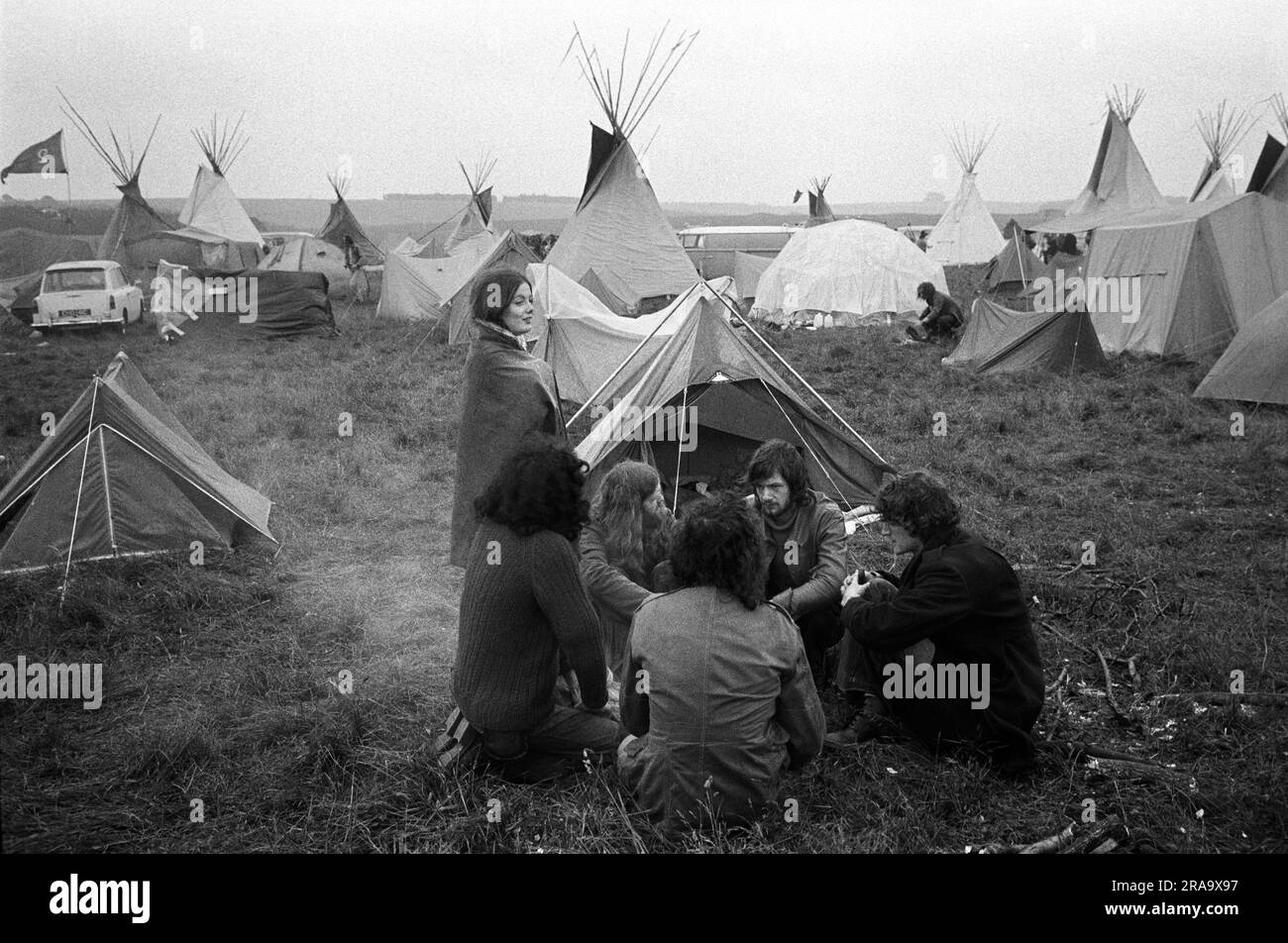 Tent village at Stonehenge Free Festival at the summer solstice, Wiltshire, England circa June 1976.  A small group of festival goers, its a three day event keep warm around a camp fire. 1970s UK HOMER SYKES Stock Photo