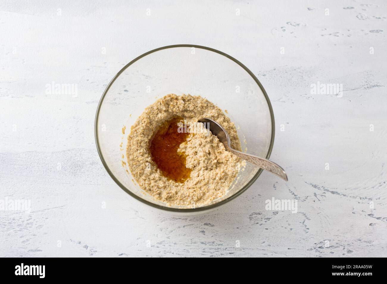 Glass bowl with soaked oatmeal and honey on a light blue table, top view. Cooking delicious healthy vegan dessert or other dish. Stock Photo